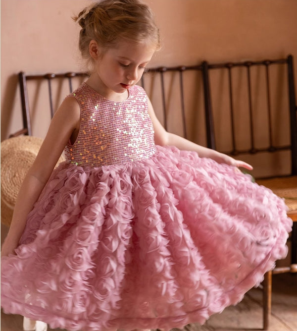 A young girl wearing a pink sequined flower dress with a fluffy skirt and a shimmering bodice adorned with sequins.