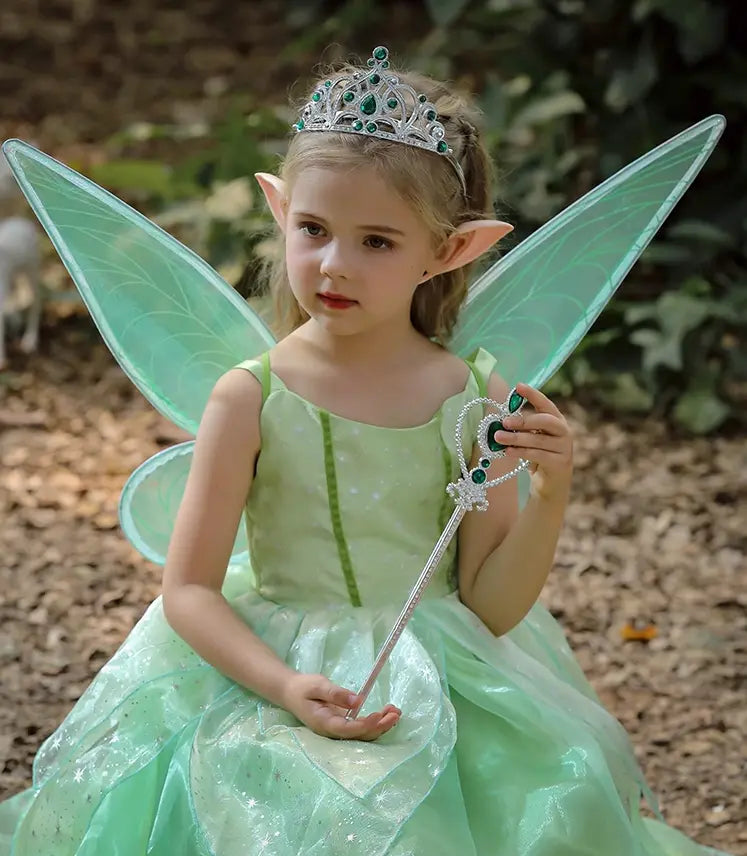 Child wearing a green fairy costume with a red bow outdoors.