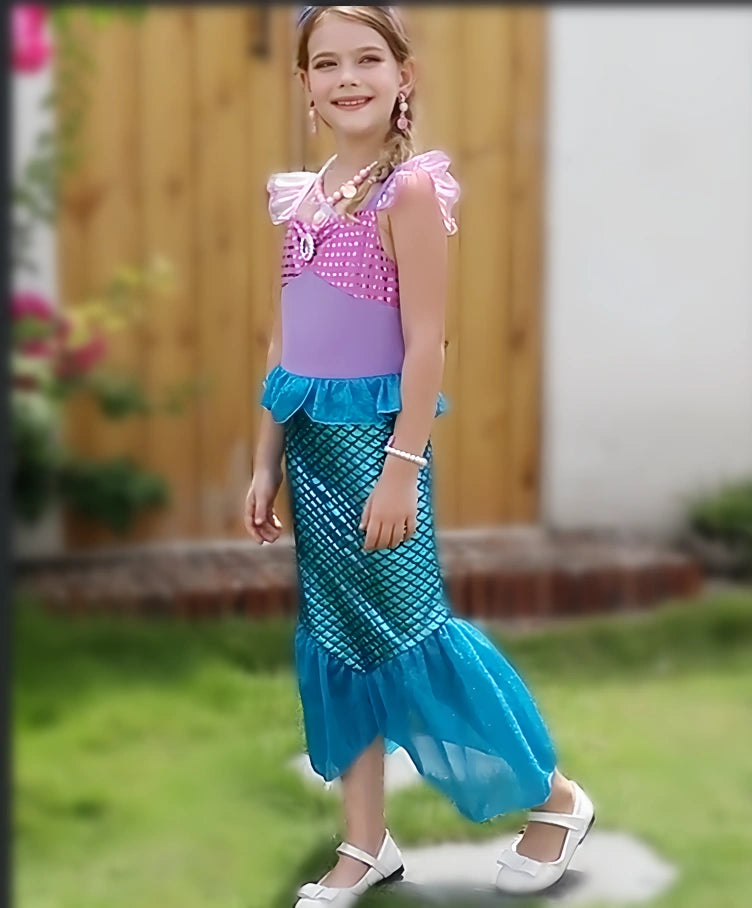 Child wearing a mermaid-themed dress with a purple top and blue tail in an outdoor setting.