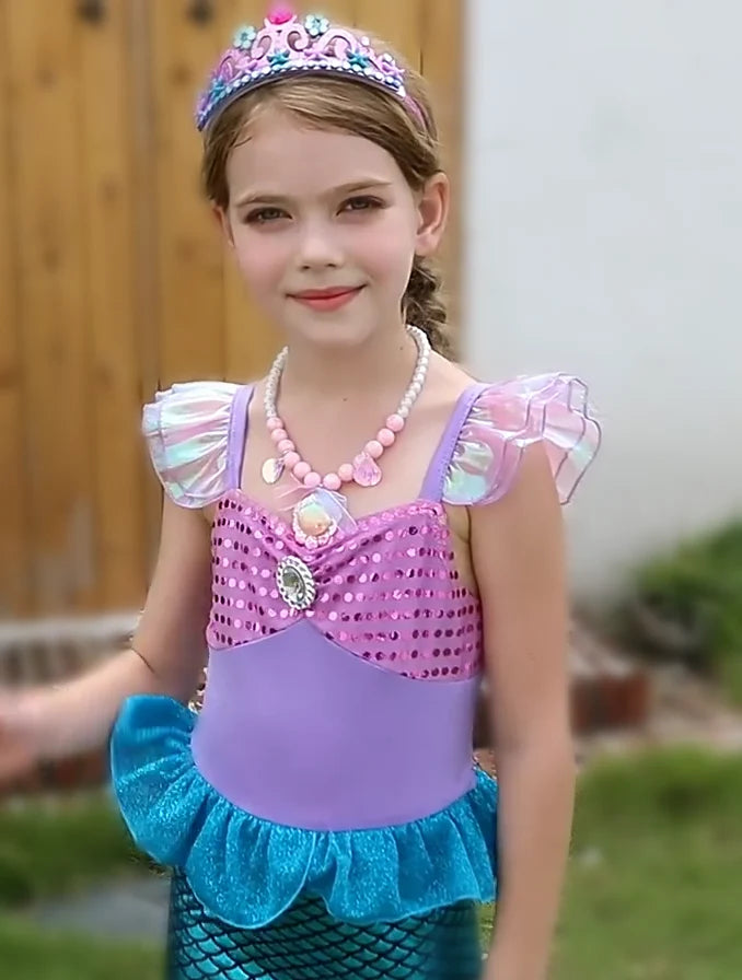 Young girl in a mermaid costume with a crown and necklace outdoors.