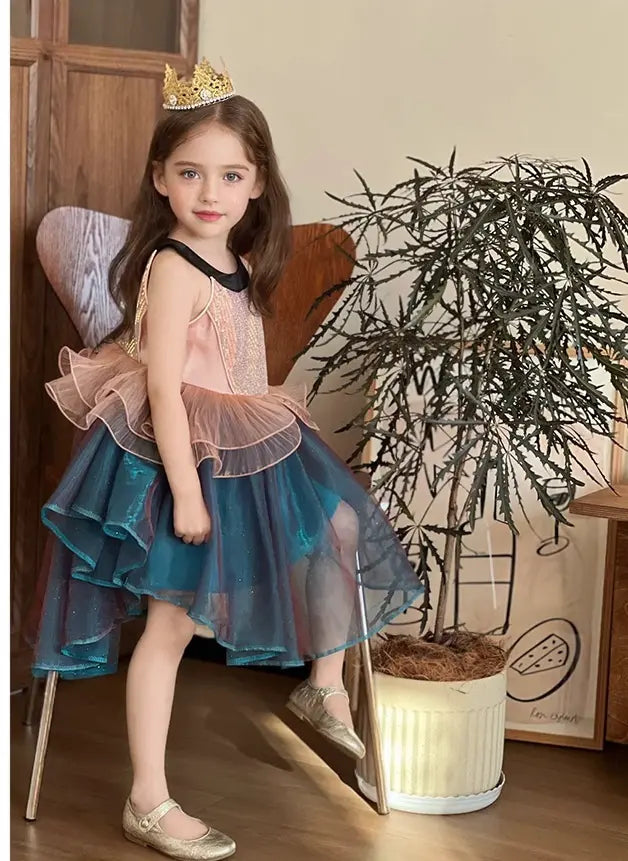 Young girl in a fairy Sleeveless Sea Princess Sequin Blue Tulle  Mermaid   costume with a blue dress and pink wings, sitting on a chair indoors.