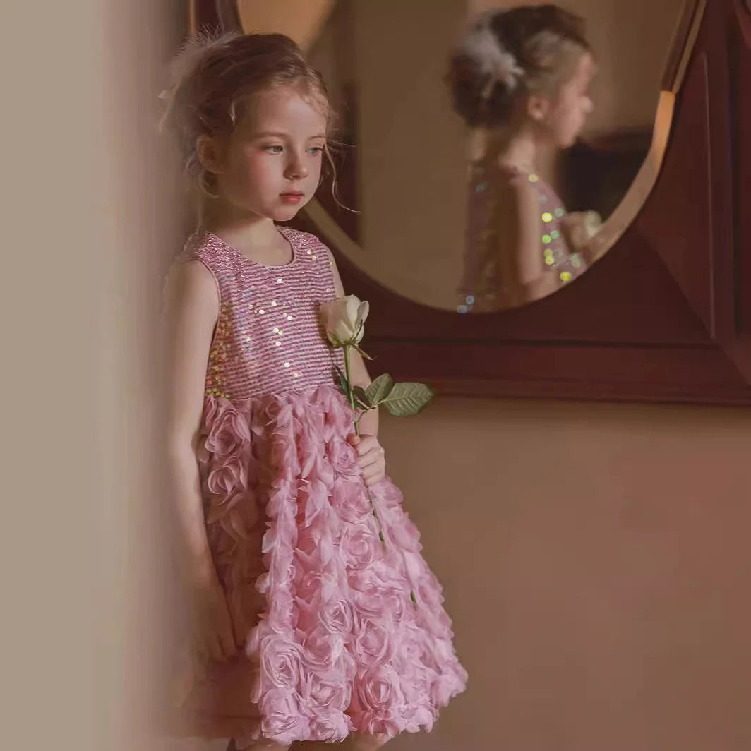 Young girl in a pink dress with floral details standing in front of a mirror.