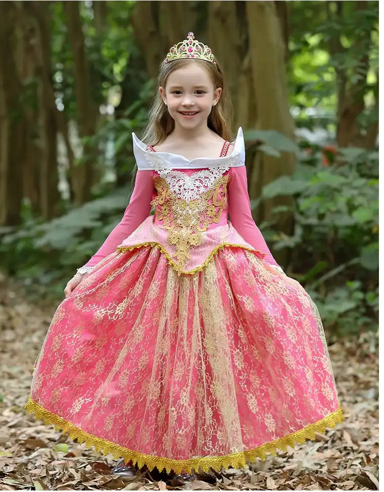 Young girl in a Princess Aurora Pink Lace Ball Gown with gold accents standing in a forest.