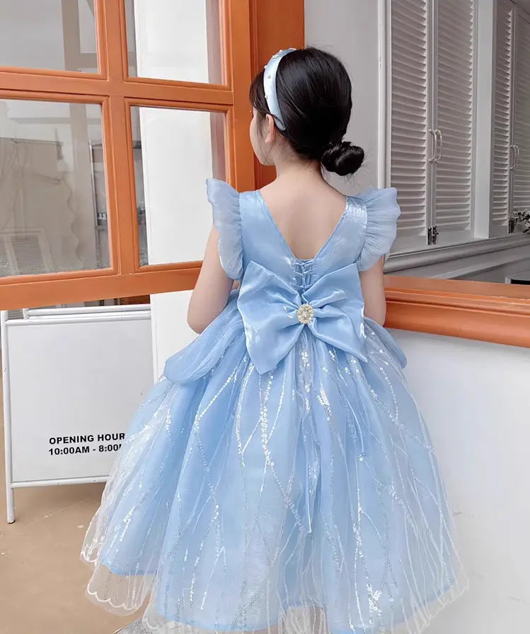 Child wearing a light Blue Fairy Princess Tulle Party Gown with a large bow in front of a window.