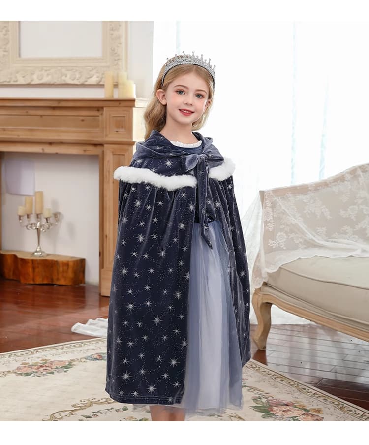 Young girl in a dark blue velvet cape with star patterns and a light gray tulle skirt, standing in a room with wooden floor and white walls.