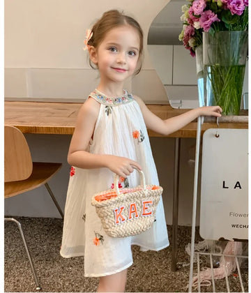 Young girl in a white Sleeveless summer  dress holding a basket with 'KAE' on it, standing in a modern interior setting.