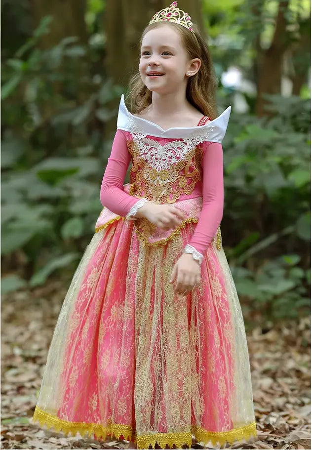 Young girl in a pink and gold Girls Pink Royal Lace Ball Gown with a tiara standing in a forest.