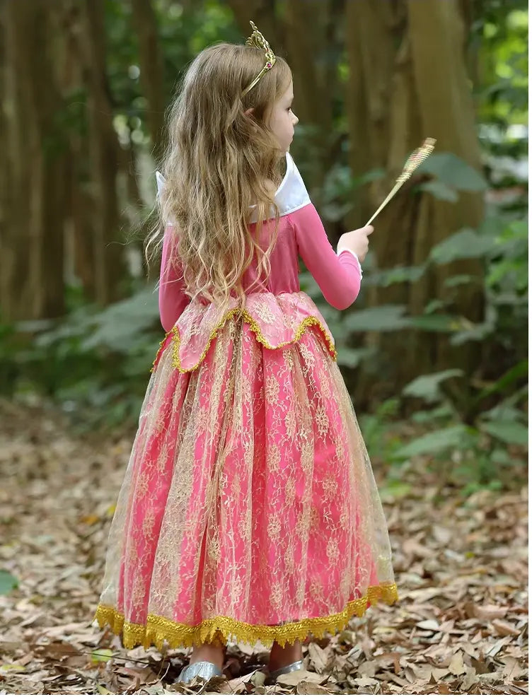 Young girl in a pink dress with gold accents standing in a forest.