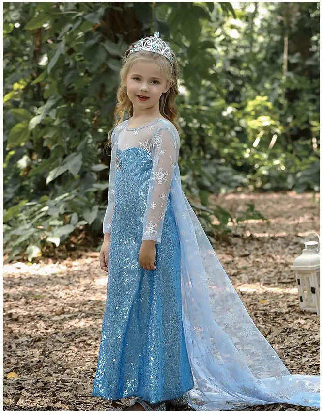 Young girl in a Glittering Winter Queen Blue Sequin Gown for Girls with Snowflake Cape with a tiara standing outdoors.