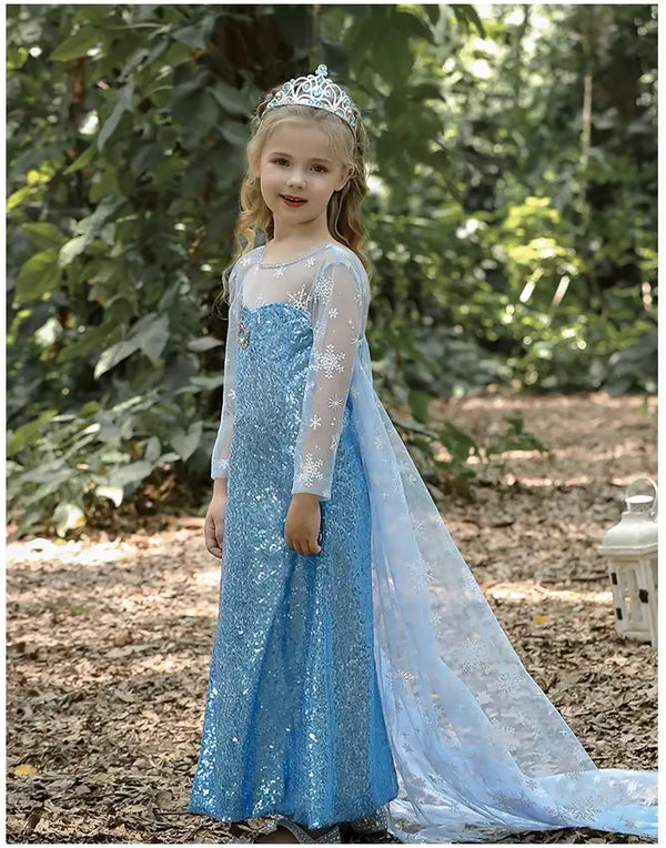 Young girl in a Glittering Winter Queen Blue Sequin Gown for Girls with Snowflake Cape with a tiara standing outdoors.