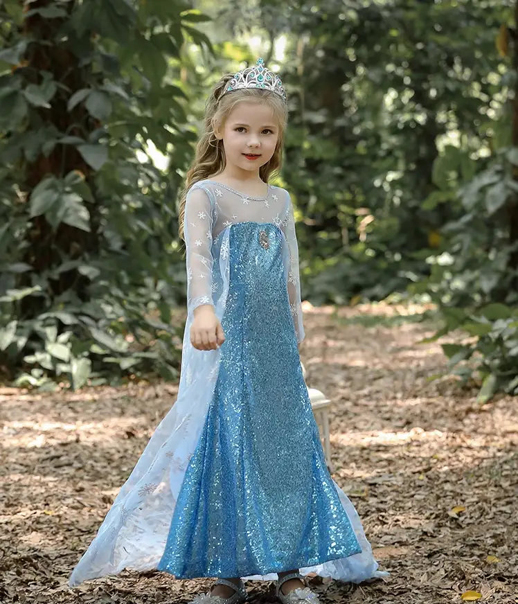 Young girl in a Glittering Winter Queen Blue Sequin Gown with Snowflake Cape  with a tiara standing in a forest setting