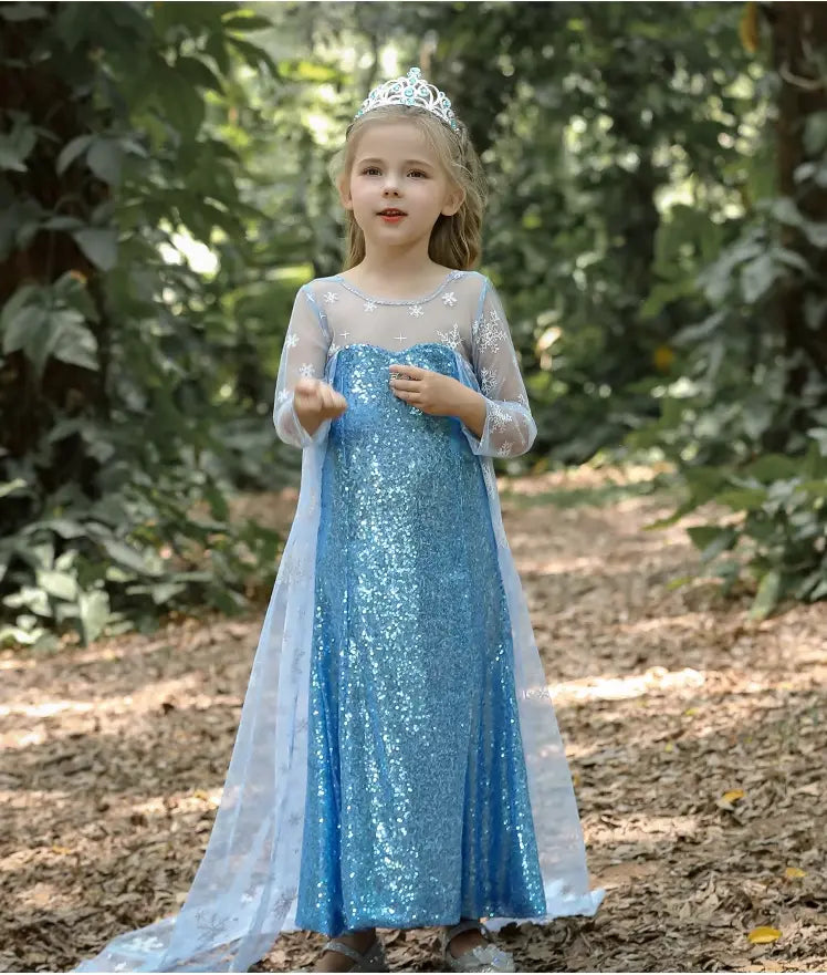 Child in a Glittering Winter Queen Blue Sequin Gown for Girls with Snowflake Cape with a tiara standing in a forest