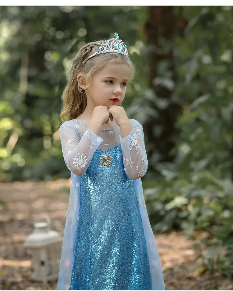 Young girl in a Glittering Winter Queen Blue Sequin Gown for Girls with Snowflake Cape  with a tiara outdoors.