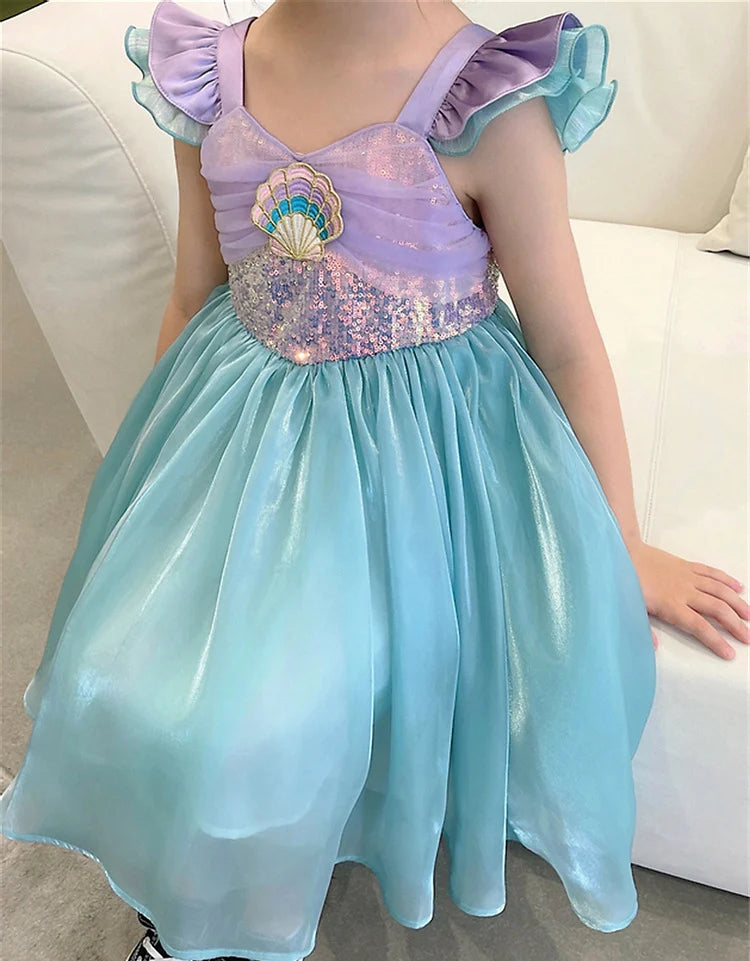 Child wearing a mermaid-themed dress with a shell design on a white couch.