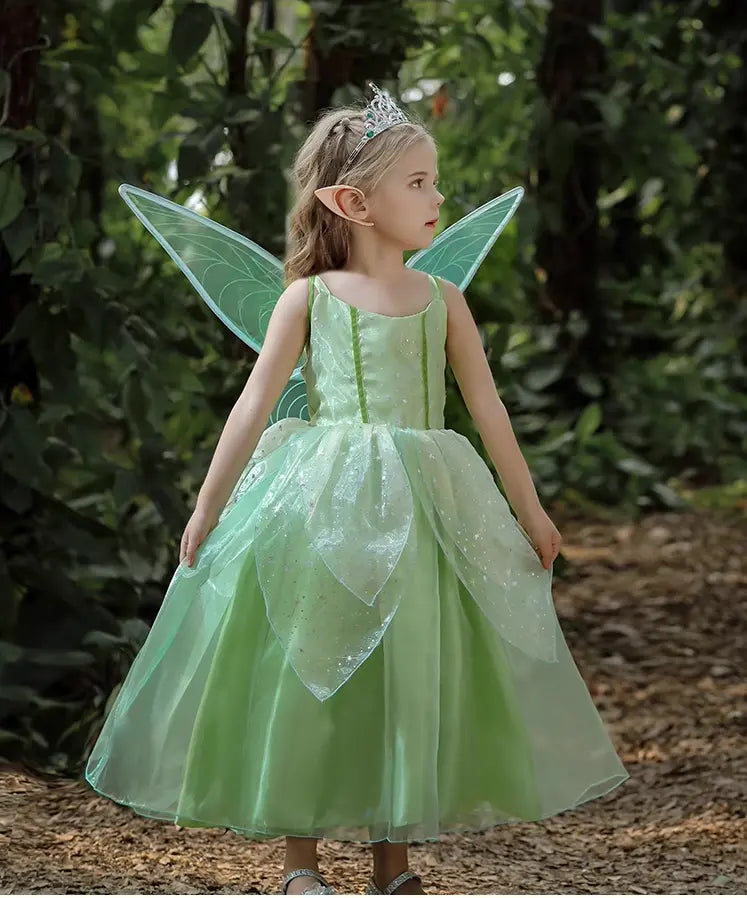 Child in a green fairy costume with wings and tiara standing in a forest setting