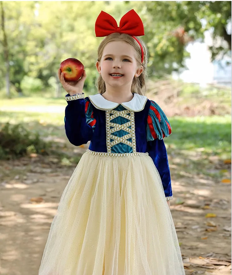 Child in Snow White costume holding an apple outdoors.