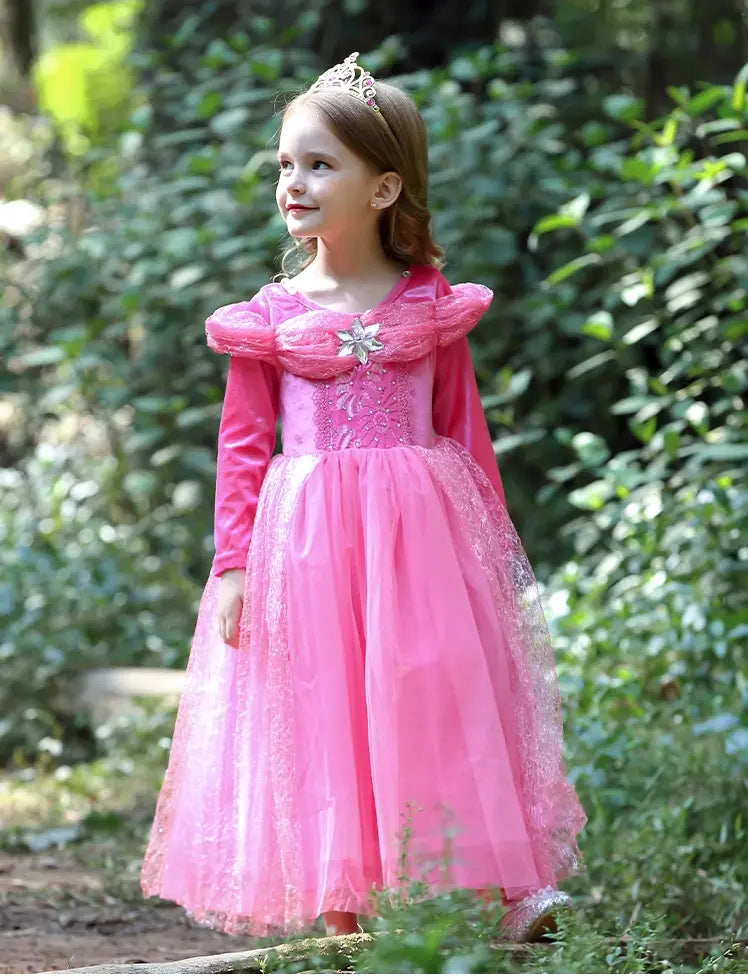 Young girl in a pink sleeping beauty princess dress with a floral headband standing in a forest.