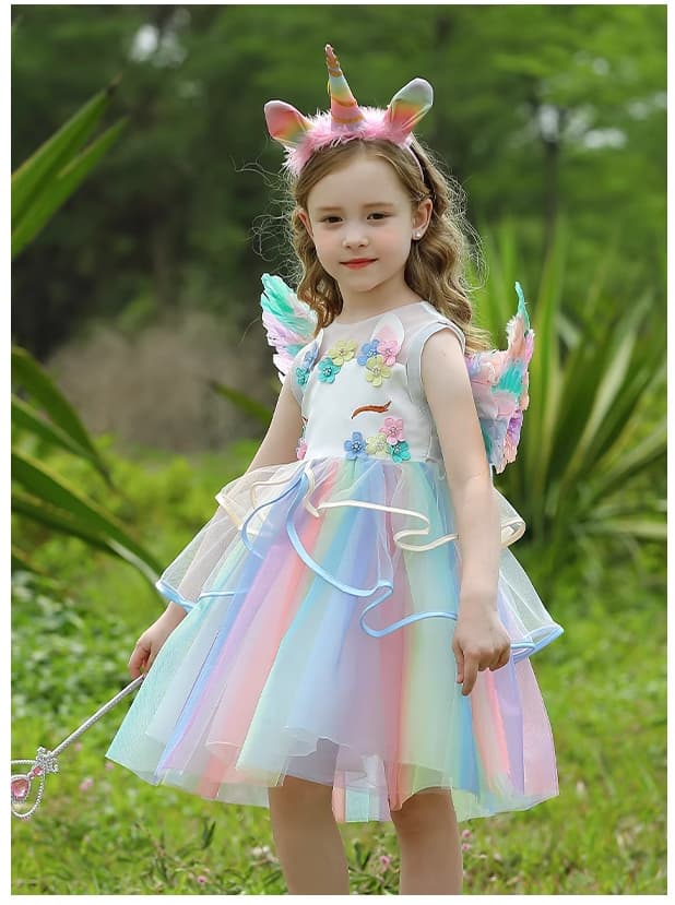Young girl in a Rainbow Unicorn Fairy Dress costume with wings and horn standing outdoors.