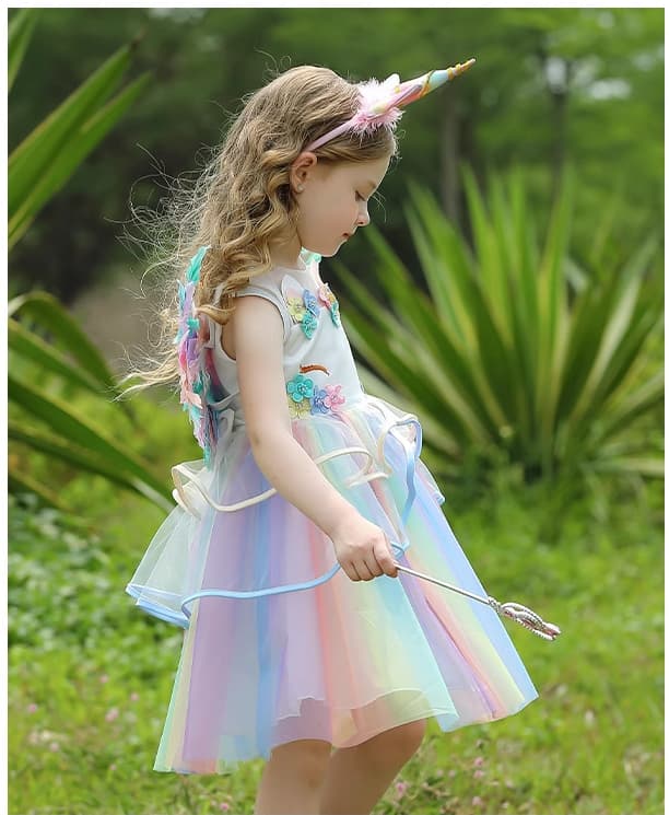 Young girl in a unicorn-themed dress holding a wand in a grassy outdoor setting