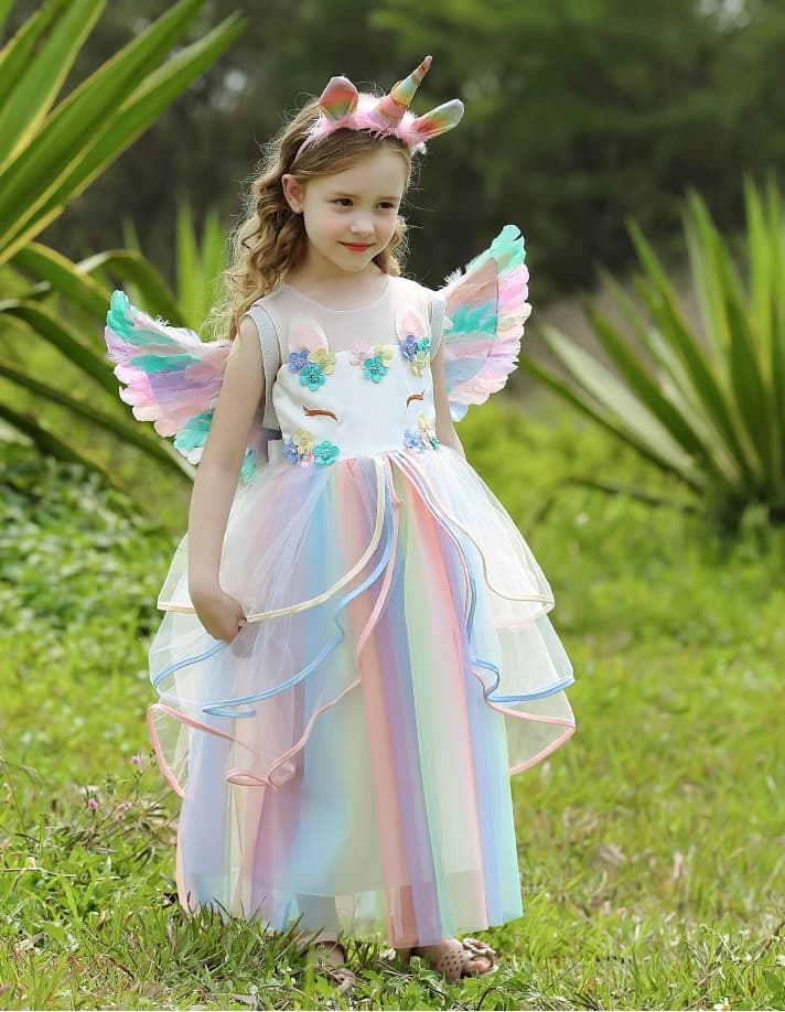 Child in a unicorn costume with wings and horn standing in a grassy area.