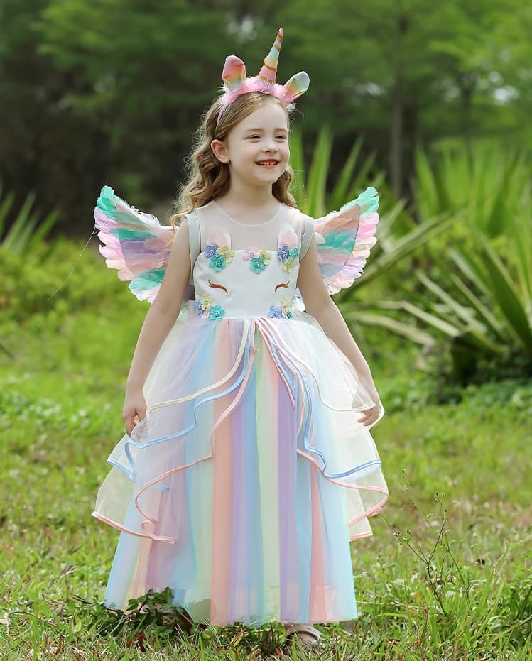 Young girl in a unicorn costume with wings and headband standing outdoors.