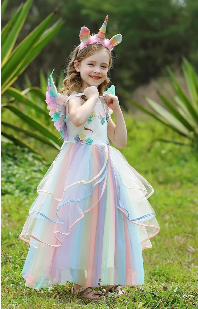 Young girl in a unicorn-themed dress with wings and headband standing outdoors.