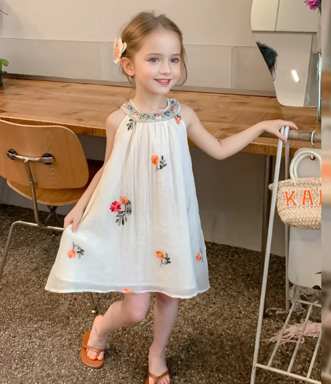 Young girl in a white Sleeveless summer dress  with floral embroidery standing in a kitchen.