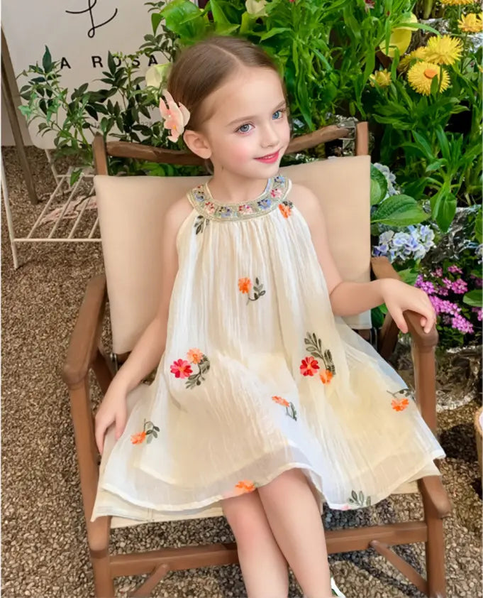 Young girl in a floral Sleeveless summer dress  sitting on a chair with flowers and plants in the background
