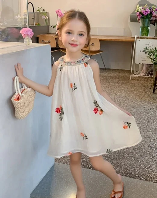 Young girl in a white Sleeveless summer dress   with floral embroidery standing in a room.