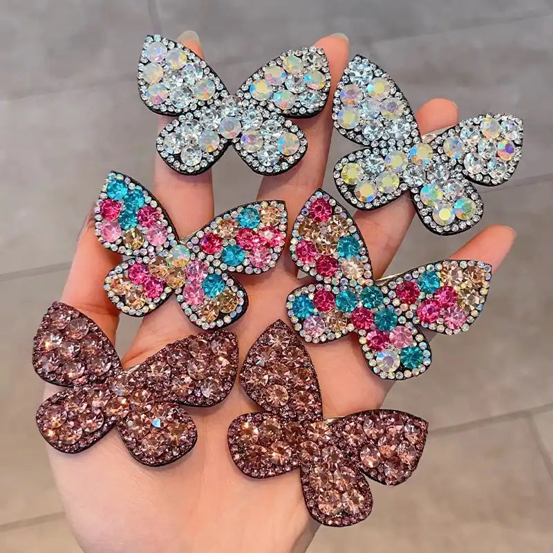 Butterfly-shaped jewelry pieces with colorful rhinestones held in a hand.