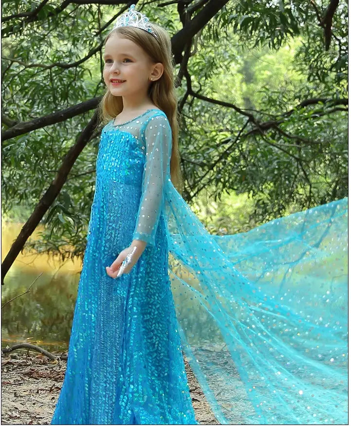 Child in a Sparkling Ice Queen Blue Sequin Gown for Girls with Sheer Cape  with long sleeves and a tiara standing in a forest.