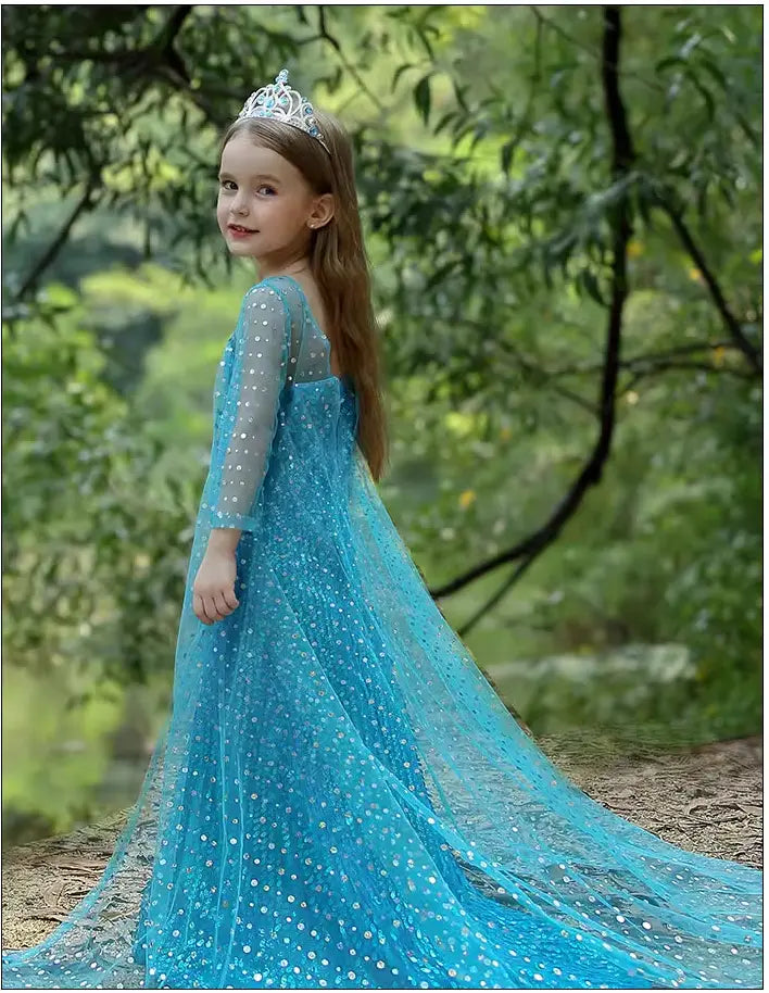 Young girl in a Sparkling Ice Queen Blue Sequin Gown for Girls with Sheer Cape  with a tiara standing in a forest.