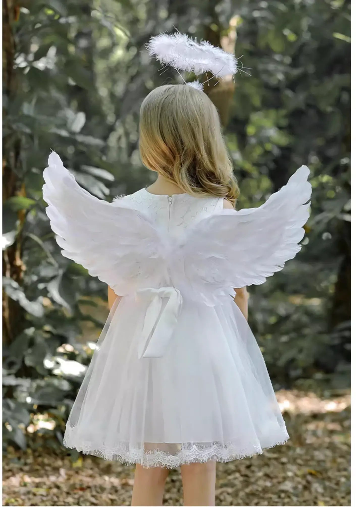 Child wearing angel wings outdoors with greenery in the background