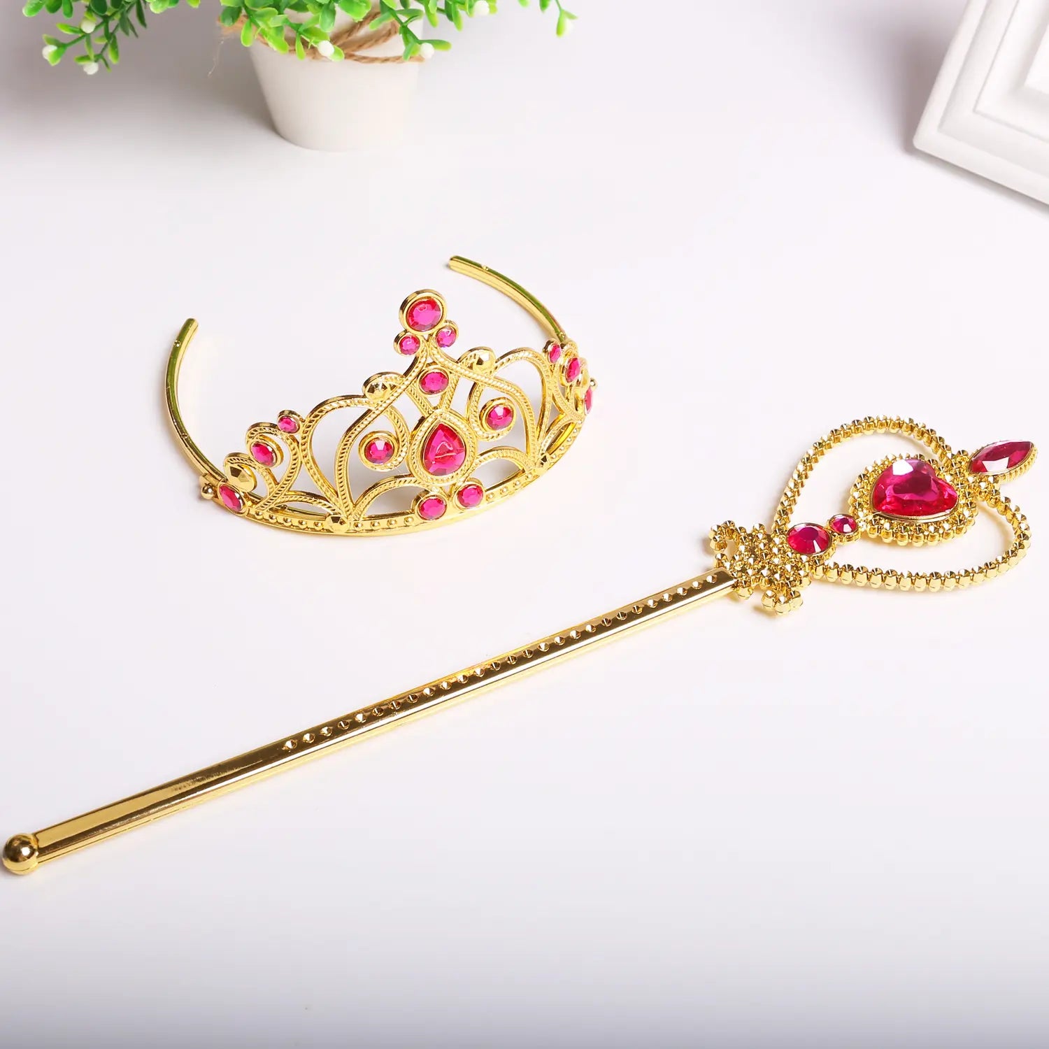 Gold tiara and wand with pink gemstones on a white background