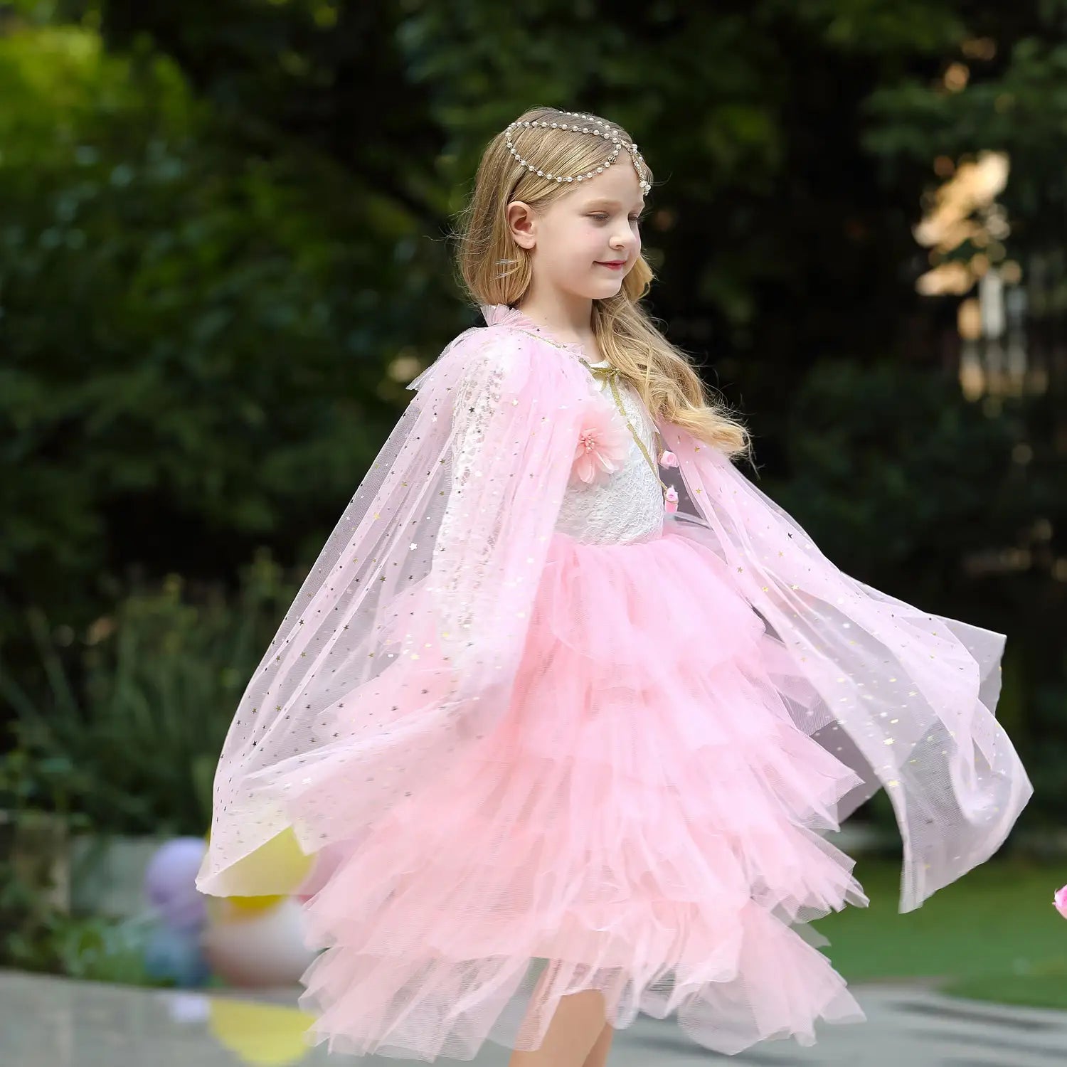 Young girl in a pink Star Tulle Fairy Dress Up Princess Cape with a blurred outdoor background