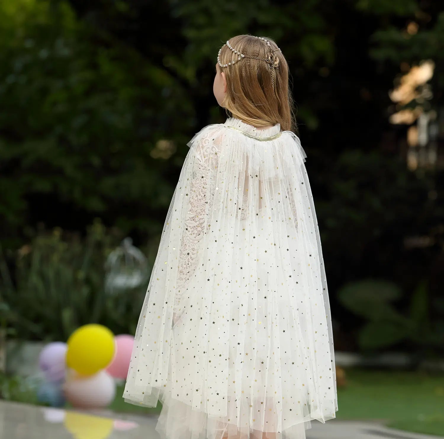 Person wearing a white Star Tulle Fairy Dress Up Princess Cape  with a blurred outdoor background