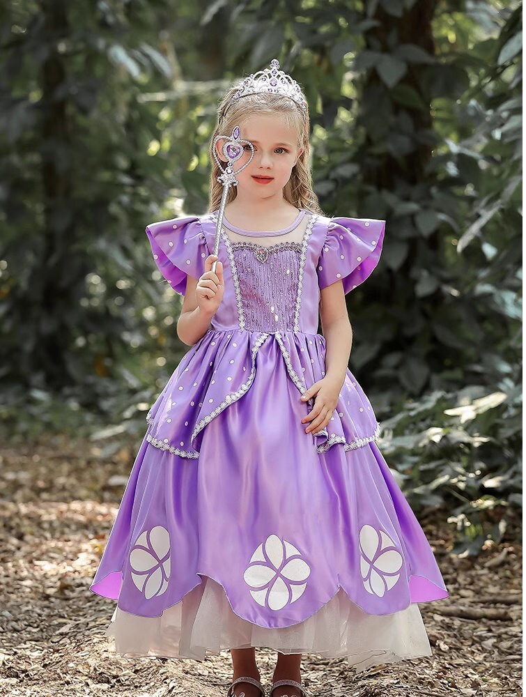 A girl dressed in an elegant purple gown with intricate floral accents and a sparkling tiara stands poised in a wooded scene, radiating royal charm and youthful grace